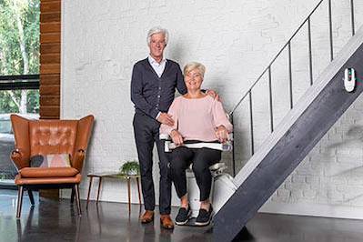 man is standing next to woman who is sitting on a stair lift