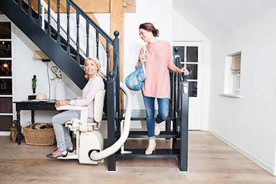 A woman who is sitting on a stair lift and a younger woman is coming down the stairs